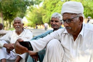An elder man listening the 2025-26 federal budget live on his mobile phone at a roadside in the Federal Capital