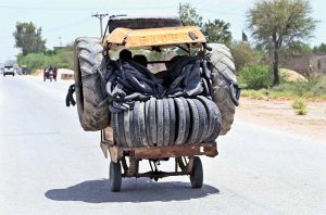 An overloaded rickshaw with old, damaged tires moves along Miro Khan Road under the scorching summer sun.
