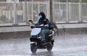 female commuter rides an electric scooter through heavy rain as the monsoon spell hits the city.