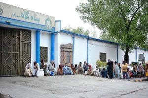 A large number of people sit outside a shelter waiting for food at the General Bus Stand