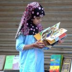 A little girl selecting old books at a roadside stall near Regal Chowk.