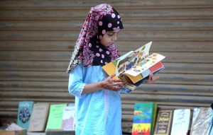A little girl selecting old books at a roadside stall near Regal Chowk.