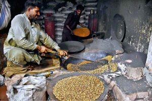 A man roasts black chickpeas for customers at his roadside setup