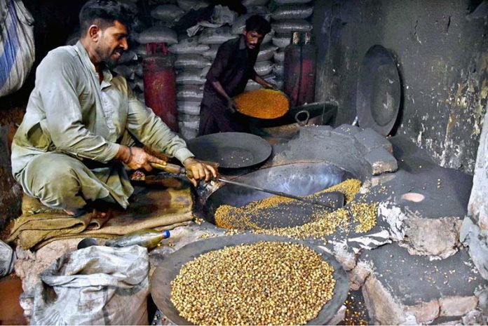 A man roasts black chickpeas for customers at his roadside setup