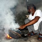 A worker busy in polishing copper pots at his workplace.