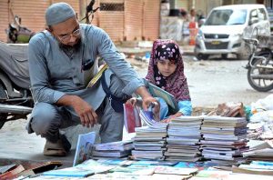 A little girl selecting old books at a roadside stall near Regal Chowk.