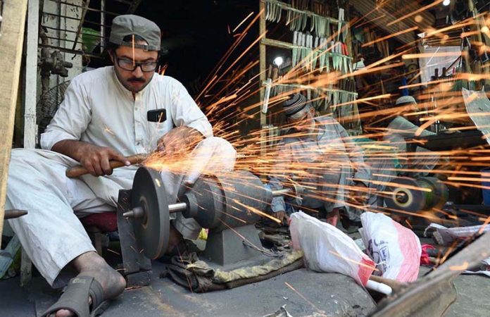A man sharpens knives to slaughter sacrificial animals in connection with upcoming Eid-ul-Adha at Firdous area