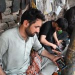 A cobbler watching the 2025-26 federal budget live on his Mobile screen at his workplace