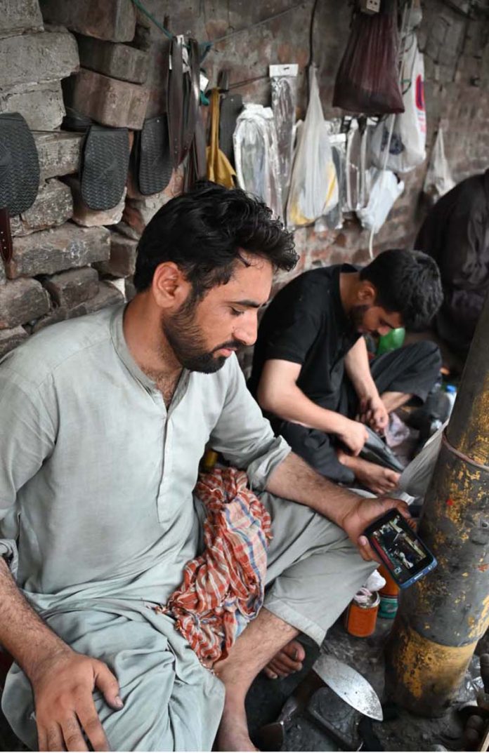 A cobbler watching the 2025-26 federal budget live on his Mobile screen at his workplace