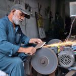A skilled worker is sharpening knives to prepare meat for the Eid al-Adha