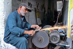A skilled worker is sharpening knives to prepare meat for the Eid al-Adha