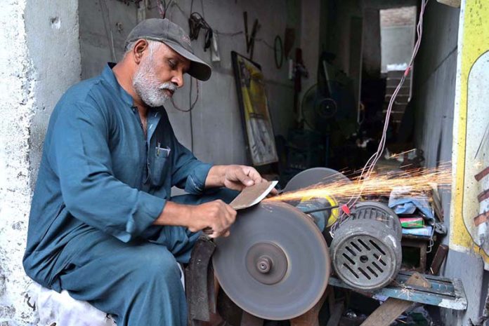 A skilled worker is sharpening knives to prepare meat for the Eid al-Adha