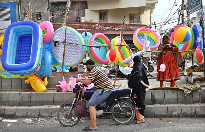A woman sells inflatable children's swimming pools, air-filled toys, and other items at a roadside stall amid high demand during summer vacations in the city