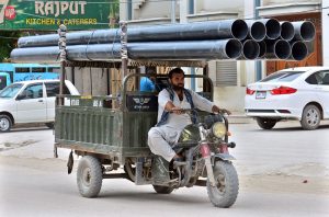 Tricycle rickshaw holder on the way loaded with plastic pipes at Latifabad