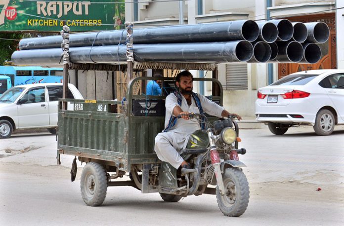 Tricycle rickshaw holder on the way loaded with plastic pipes at Latifabad