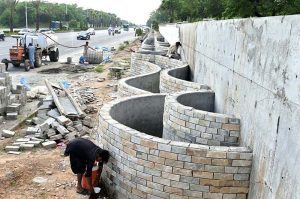 Labourers are busy construction work of a boundary wall along Srinagar Highway, part of efforts to enhance the beauty of Federal Capital