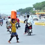 A young girl carries a water cooler on her head as she crosses the road after filling it from a filtration plant during hot day in the city