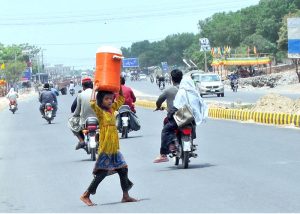 A young girl carries a water cooler on her head as she crosses the road after filling it from a filtration plant during hot day in the city