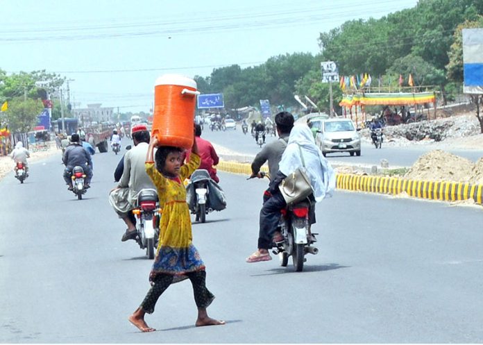 A young girl carries a water cooler on her head as she crosses the road after filling it from a filtration plant during hot day in the city