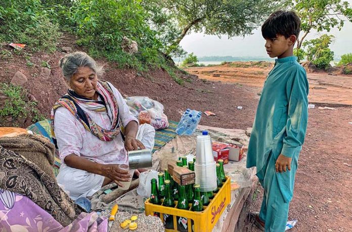 An elderly woman vendor prepares a summer drink for customers at her roadside stall in the Federal Capital