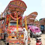 Workers are busy decorating a truck with colorful stickers and other decorative items at their workshop near IJP Road