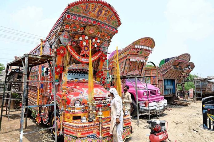 Workers are busy decorating a truck with colorful stickers and other decorative items at their workshop near IJP Road