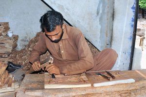 A worker is busy carving designs on a wooden sheet at his workplace, showcasing traditional craftsmanship.