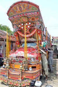 Workers are busy decorating a truck with colorful stickers and other decorative items at their workshop near IJP Road