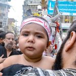 A man having a minor attend the mourning procession of 10th Muharram ul Harram, to commemorate the death anniversary of Hazrat Imam Hussein, the grandson of prophet Muhammad (PBUH) and his companion, who were martyred in the battle of Karbala, Iraq