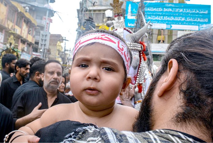 A man having a minor attend the mourning procession of 10th Muharram ul Harram, to commemorate the death anniversary of Hazrat Imam Hussein, the grandson of prophet Muhammad (PBUH) and his companion, who were martyred in the battle of Karbala, Iraq