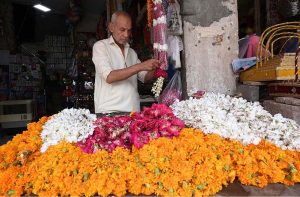 An old man busy in making flower garlands for a customer at Fawara Chowk