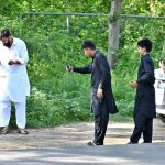 A family captures video with their cell phones as a person feeds corn to a monkey on Margalla Road in the Federal Capital