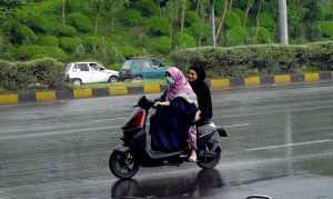 Girls riding a scooty move along the Expressway during rainfall in the Federal Capital.