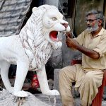 A skilled person carving a replica of lion at his roadside workshop to attract the customers at 17Mil area