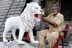 A skilled person carving a replica of lion at his roadside workshop to attract the customers at 17Mil area