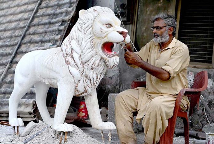 A skilled person carving a replica of lion at his roadside workshop to attract the customers at 17Mil area