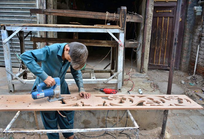A young worker busy in preparing design on the wood with help of machine at his workplace