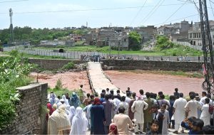 A large crowd has gathered along the Korang Nullah at Sharifabad in the Federal Capital as water levels rose following recent rains. Security personnel are preventing people from crossing the bridge after a young man drowned in the nullah