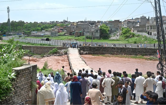 A large crowd has gathered along the Korang Nullah at Sharifabad in the Federal Capital as water levels rose following recent rains. Security personnel are preventing people from crossing the bridge after a young man drowned in the nullah