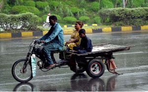 Girls riding a scooty move along the Expressway during rainfall in the Federal Capital.