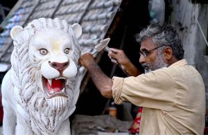 A skilled person carving a replica of lion at his roadside workshop to attract the customers at 17Mil area