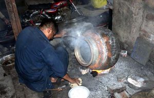 A worker puts the finishing touches on iron pots (digins) used for large banquets, over a roaring fire at an iron factory near Mochi Gate