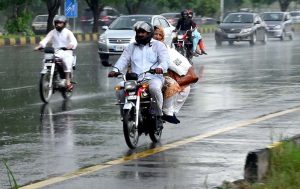 Girls riding a scooty move along the Expressway during rainfall in the Federal Capital.