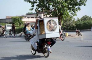 Motorcyclists dangerously carry room coolers on the back seat, risking safety on busy city road.