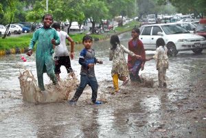 A man and his child take shelter under an umbrella to stay dry during the monsoon downpour in the Federal Capital