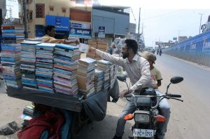 A motorcyclist purchases old books from a roadside vendor in the Korangi area.