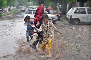 A man and his child take shelter under an umbrella to stay dry during the monsoon downpour in the Federal Capital