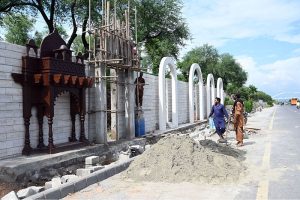 Labourers busy in construction work on a wall along Srinagar Highway to enhance the city's aesthetic appeal in the Federal Capital.