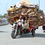 An overloaded loader rickshaw navigates the Railway Overbridge Road, reflecting unsafe commuting practices on busy routes in the city