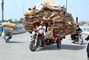 An overloaded loader rickshaw navigates the Railway Overbridge Road, reflecting unsafe commuting practices on busy routes in the city